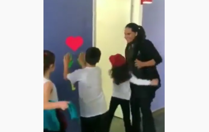 Estagiária incentiva crianças com cumprimentos antes das aulas e vídeo viraliza Crianças podem escolher receber um abraço, fazer uma dança ou toque de mãos