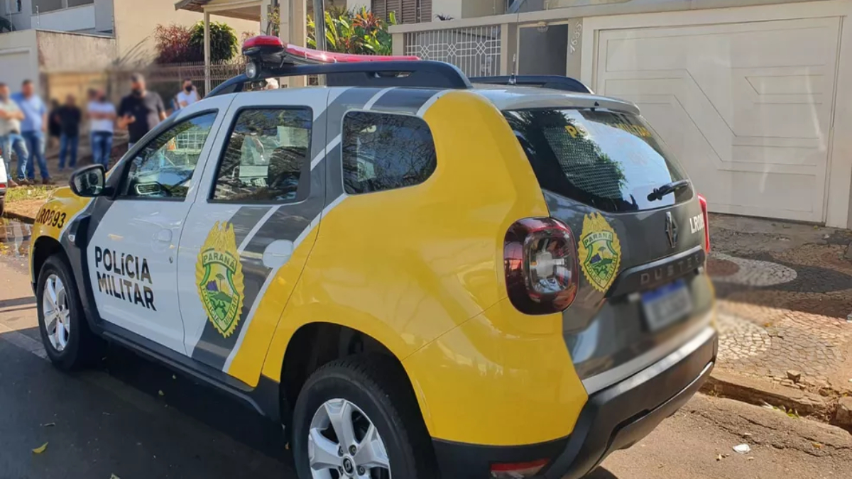 Viatura da polícia, nas cores branco, cinza e amarelo. O veículo está proximo a casa onde aconteceu um triplo homicídio contra uma família. 