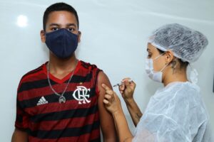 Profissional de saúde aplica vacina contra Covid-19 em adolescente com camisa do Flamengo