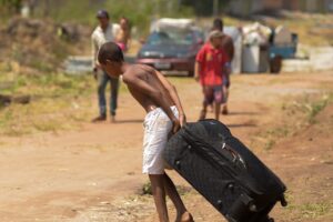 Criança puxa uma mala em terreno de chão batido a ocupação