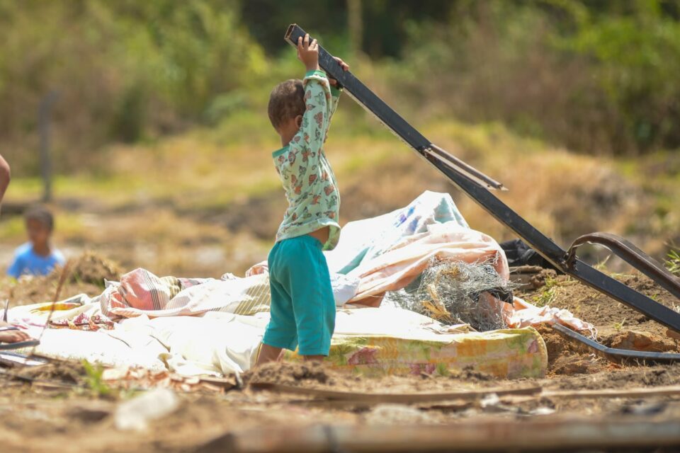 Criança levanta objeto em meio a escombros de de ocupação em Aparecida de Goiânia