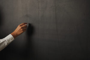 Pessoa escreve em quadro negro - A mãe de um aluno é suspeita de arremessar um livro contra uma professora durante uma reunião, em escola da cidade de Paraúna. Saiba mais!