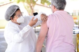 Profissional de saúde aplica vacina em braço de idoso