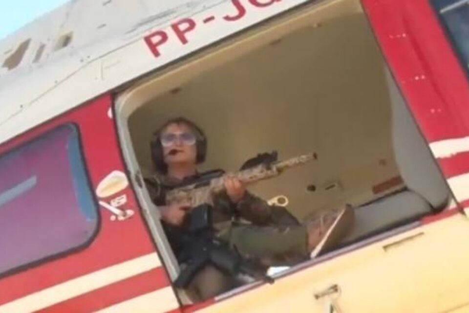 Magda Mofatto em helicóptero segurando rifle