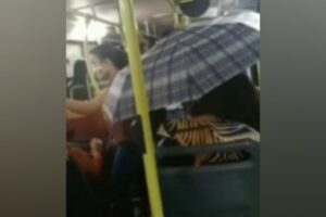Uma mulher teve que usar um guarda-chuva para se proteger de uma goteira em um ônibus, em Goiânia, na última terça-feira (30). (Foto: reprodução/TV Anhanguera)
